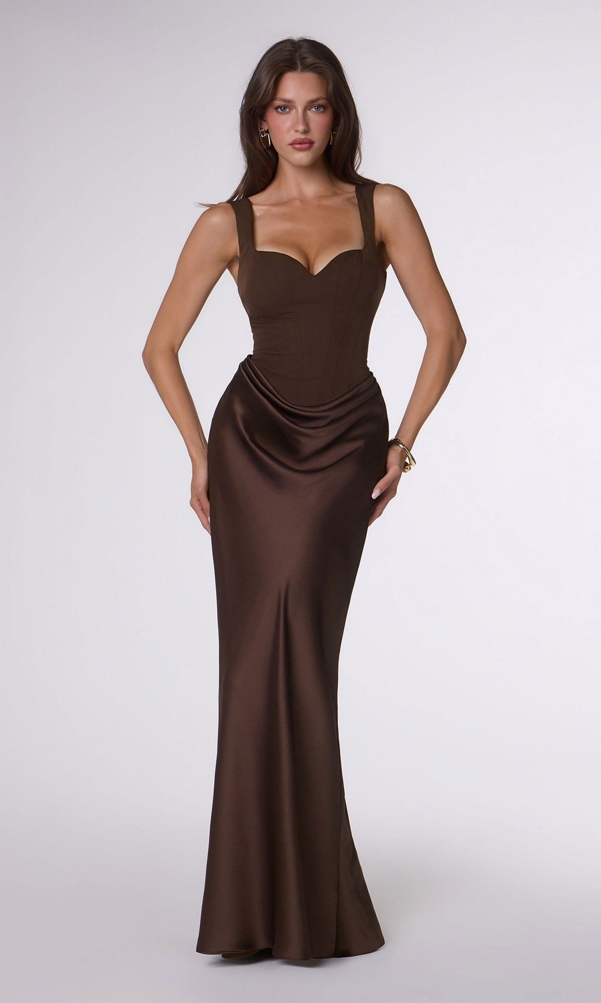 A woman stands facing forward in the Amoris T742—a fitted, floor-length dark brown satin prom dress with wide straps, a sweetheart neckline, and an adjustable lace-up back—against a plain white background.